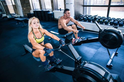couple working abs and upper body on a rowing machines at the gym