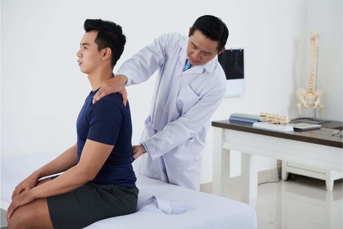 Physician assessing the spine and back of a male adult patient