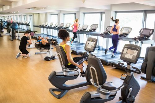 people working out in a gym, some using a recumbent bike and some using a treadmill